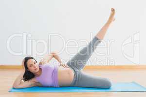 Smiling pregnant woman lying on mat lifting her leg