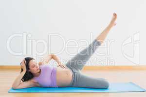 Smiling pregnant brunette lying on mat lifting her leg
