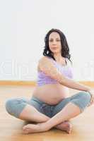 Pregnant brunette sitting on floor in lotus pose stretching