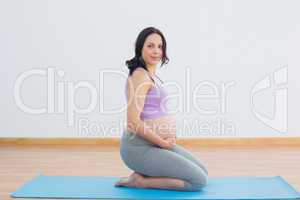 Pregnant brunette kneeling on exercise mat smiling at camera
