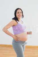 Pregnant woman holding bottle of water smiling at camera