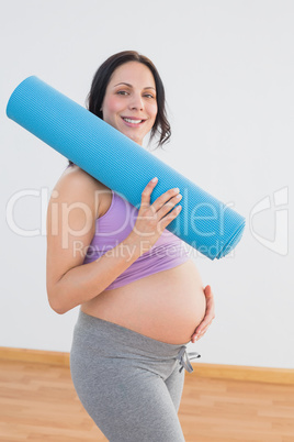 Pregnant woman holding exercise mat smiling at camera