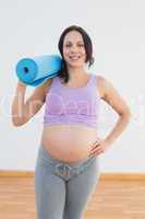 Happy pregnant woman holding exercise mat smiling at camera