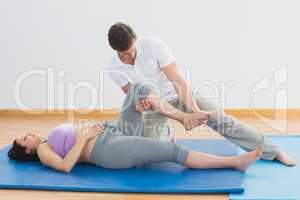 Masseur moving pregnant womans leg on blue mat