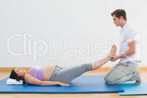Masseur lifting pregnant womans legs on blue mat