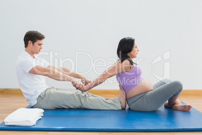 Masseur stretching pregnant womans arms and shoulders on a mat