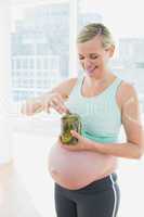 Blonde pregnant woman eating from jar of pickles