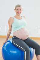 Happy blonde pregnant woman sitting on blue exercise ball