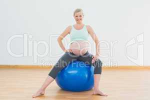 Smiling blonde pregnant woman sitting on blue exercise ball