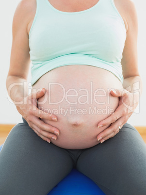 Pregnant woman sitting on blue exercise ball holding her belly