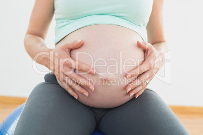 Pregnant woman sitting on exercise ball holding her belly