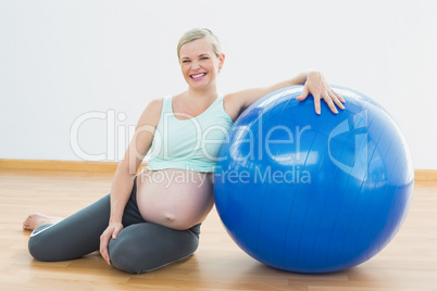 Pregnant woman sitting beside exercise ball smiling at camera