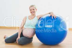 Pregnant woman sitting beside exercise ball smiling at camera
