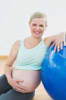 Happy pregnant woman leaning against exercise ball holding her b