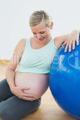 Smiling pregnant woman leaning against exercise ball holding her