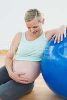 Smiling pregnant woman leaning against exercise ball holding her