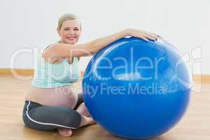 Smiling pregnant woman sitting beside exercise ball