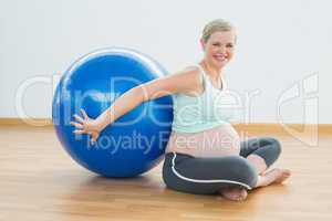 Happy pregnant woman sitting beside exercise ball