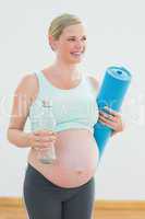 Pregnant woman holding bottle of water and exercise mat