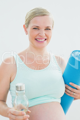 Pregnant woman holding bottle of water and exercise mat smiling