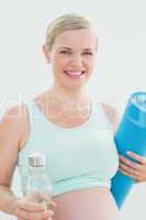 Pregnant woman holding bottle of water and exercise mat smiling