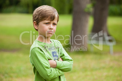 Serious boy standing with arms crossed at park