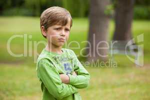 Serious boy standing with arms crossed at park