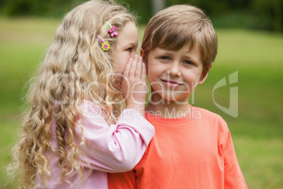 Girl whispering secret into boy's ear at park