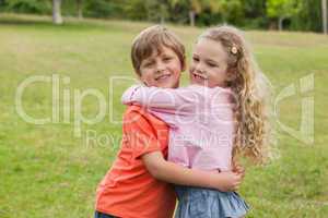 Two smiling kids hugging at park
