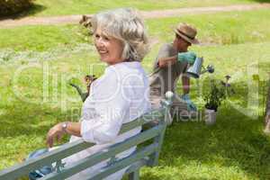 Woman on bench while man watering plant at park