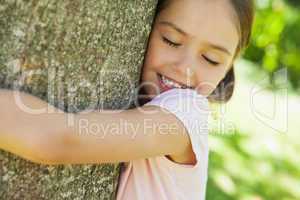 Smiling girl hugging tree with eyes closed at park