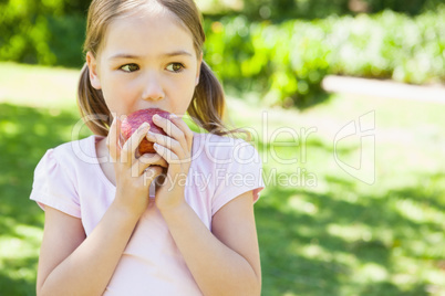 Pretty young girl eating apple in park