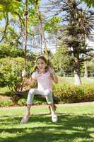 Happy young girl sitting on swing at park