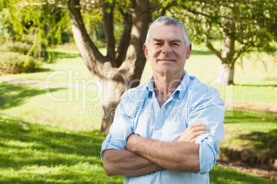 Content mature man with arms crossed at park