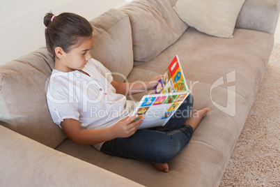 Relaxed girl reading storybook on sofa in the living room