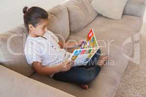 Relaxed girl reading storybook on sofa in the living room