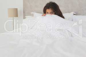 Girl hiding face behind sheet in bed