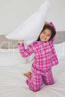 Happy young girl holding up a pillow in bed