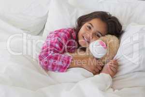 Portrait of a smiling girl with stuffed toy resting in bed