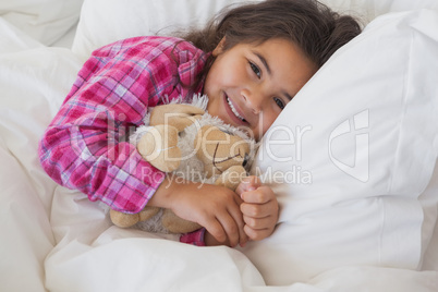 Smiling girl with stuffed toy resting in bed