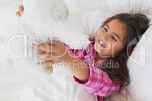 Smiling girl with stuffed toy resting in bed
