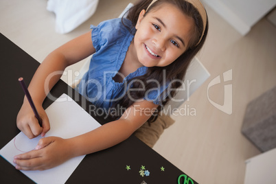 Portrait of a young smiling girl drawing on table