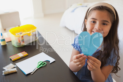 Cute young girl holding heartshape paper at table