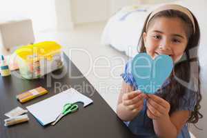 Cute young girl holding heartshape paper at table
