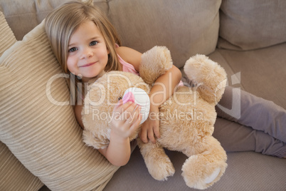 Portrait of a smiling girl with stuffed toy sitting on sofa