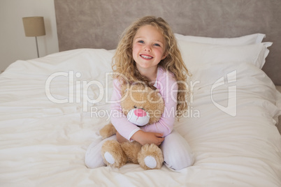 Young happy girl with stuffed toy sitting on bed