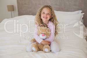 Young happy girl with stuffed toy sitting on bed