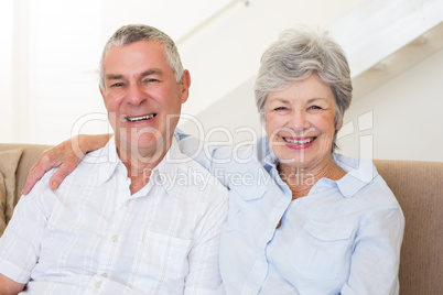 Retired couple sitting on couch smiling at camera