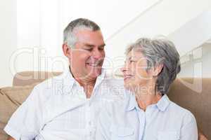 Senior couple sitting on sofa smiling at each other