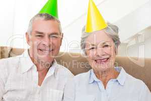 Senior couple sitting on couch wearing party hats